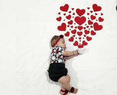 a baby laying on the ground with hearts drawn on it's wall behind her