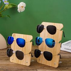 three wooden sunglasses with blue mirrored lenses sitting on top of a table next to a white flower