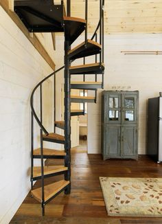 a spiral staircase in the middle of a room next to a cabinet and rug on the floor