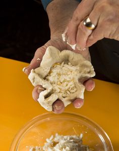 two hands are holding food in front of a yellow tablecloth and bowl with another person's hand