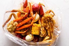 crab legs, corn on the cob and potatoes in a plastic bag sitting on a white surface