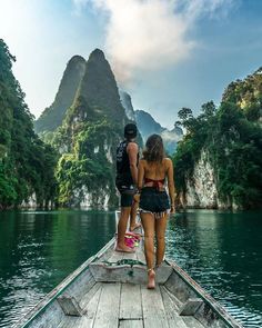 two people are standing on the end of a boat in front of mountains and water