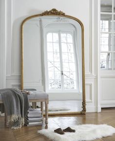 a large mirror sitting on top of a wooden floor next to a white chair and rug