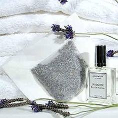 an assortment of towels and perfume bottles on a white table cloth with lavenders in the background