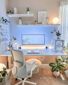 a white desk topped with a computer monitor next to a chair and potted plants