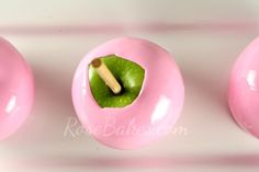 three pink donuts with green apple inside on a white surface, one has a piece of wood sticking out of it