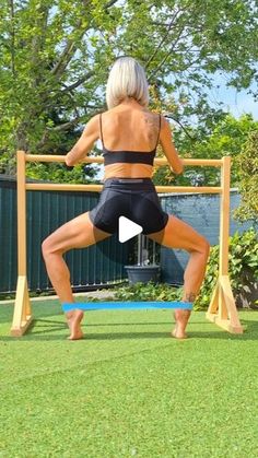 a woman in black shorts doing squats on a blue mat with a wooden frame