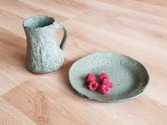 two small raspberries sit on a plate next to a ceramic pitcher and bowl