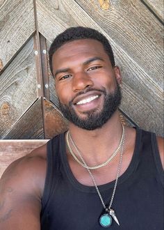 a man with a beard wearing a black tank top and silver necklace smiling at the camera