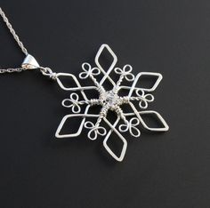 a silver snowflake necklace on a black surface with an intricate design in the center