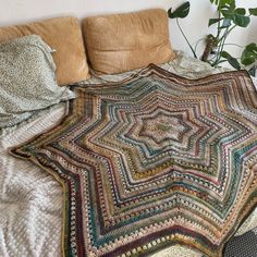 a bed with a blanket on top of it next to pillows and a potted plant