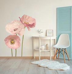 three pink flowers on a white wall next to a table and chair in a room