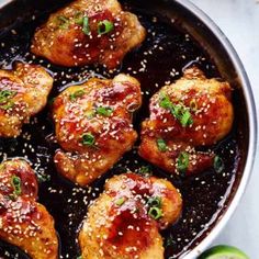 chicken thighs in a skillet with sesame seeds on the side and limes next to it