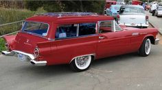 an old red car is parked on the side of the road with other cars behind it