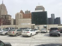 several cars are parked in a parking lot with tall buildings behind them and the city skyline