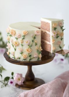 a white cake with pink and yellow flowers on it, sitting on a wooden stand