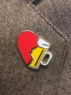 a red and yellow heart shaped pin with a beer in it's mouth on a gray jacket