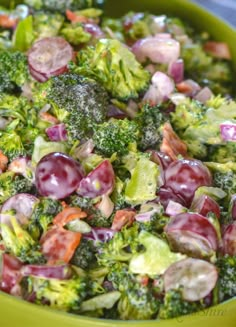 a green bowl filled with broccoli, grapes and other food items on top of a table