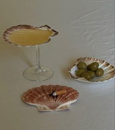 three seashells with olives and a drink on a white tablecloth covered table