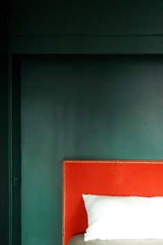 a red headboard with white pillows in a green walled bed room, against a dark green wall