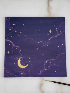 a painting with stars and the moon on it next to a paintbrush sitting on top of a table