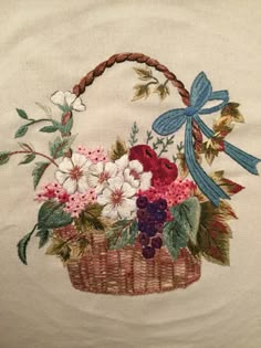 a basket filled with flowers on top of a white cloth covered wall hanging next to a blue ribbon