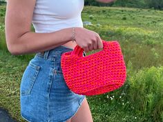 a woman holding a pink crocheted purse in her hand and looking at the camera