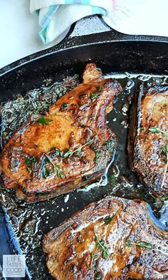 steaks cooking in a cast iron skillet with herbs on the top and bottom