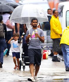 the man is walking down the street with an umbrella over his head and holding a drink