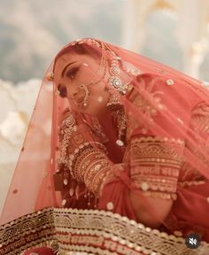 a woman in a red and gold bridal outfit looking down at her wedding veil