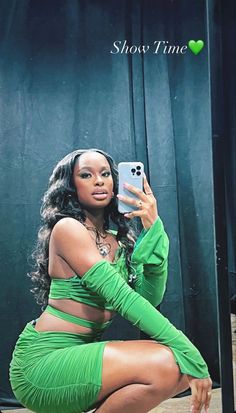 a woman in a green outfit taking a selfie with her cell phone while sitting on a stool