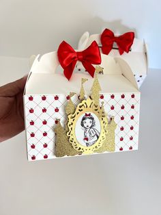 a hand holding up a small box with a picture on it and red bows around the edges