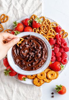 a person dipping chocolate into a bowl with pretzels and strawberries on the side