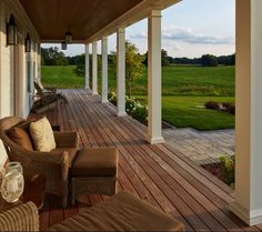 the porch is covered with wicker furniture and has an expansive green field in the background