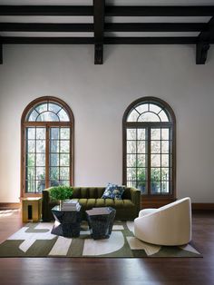 a living room with two large windows and a green couch in front of the window