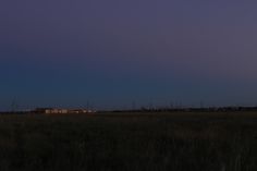 the moon is setting over an open field with power lines in the distance and buildings lit up at night