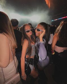 two beautiful young women standing next to each other at a concert with bright lights in the background