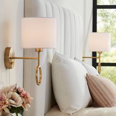 two lamps are on the wall next to a bed with white pillows and pink flowers