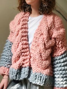 a woman is wearing a pink and blue knitted cardigan with large hoop earrings