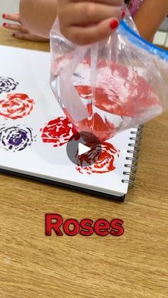 someone is painting roses on a notebook with red and blue ink, while another person's hands are holding a plastic bag