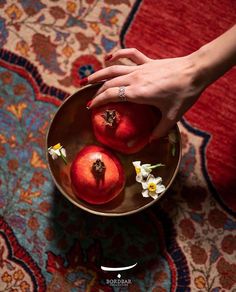 a woman's hand reaching for two pomegranates in a bowl