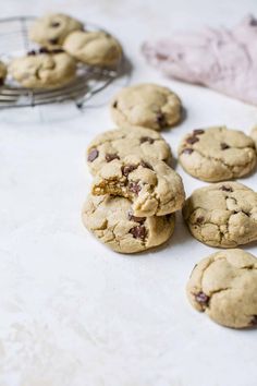 chocolate chip cookies on a white table with a cooling rack and towel in the background