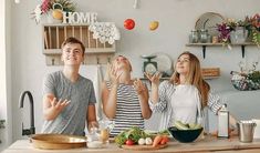 two people standing in front of a kitchen counter with food on the counter and one person looking up