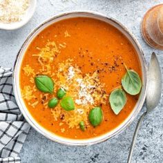 a bowl of tomato soup with basil leaves and cheese on top, next to other dishes