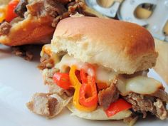 a close up of a sandwich on a plate with meat and peppers in the background