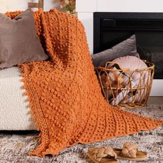 an orange crocheted blanket sitting on top of a bed next to a pair of slippers