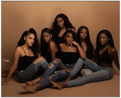 four women sitting on the floor posing for a photo together, with one woman wearing ripped jeans