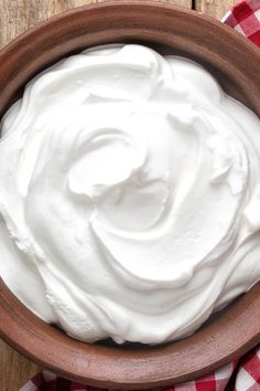 a wooden bowl filled with whipped cream on top of a checkered table cloth next to a knife