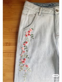 a pair of jeans with flowers embroidered on the front and back side, sitting on a wooden floor