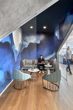 a man sitting on a couch in front of a wall with clouds painted on it